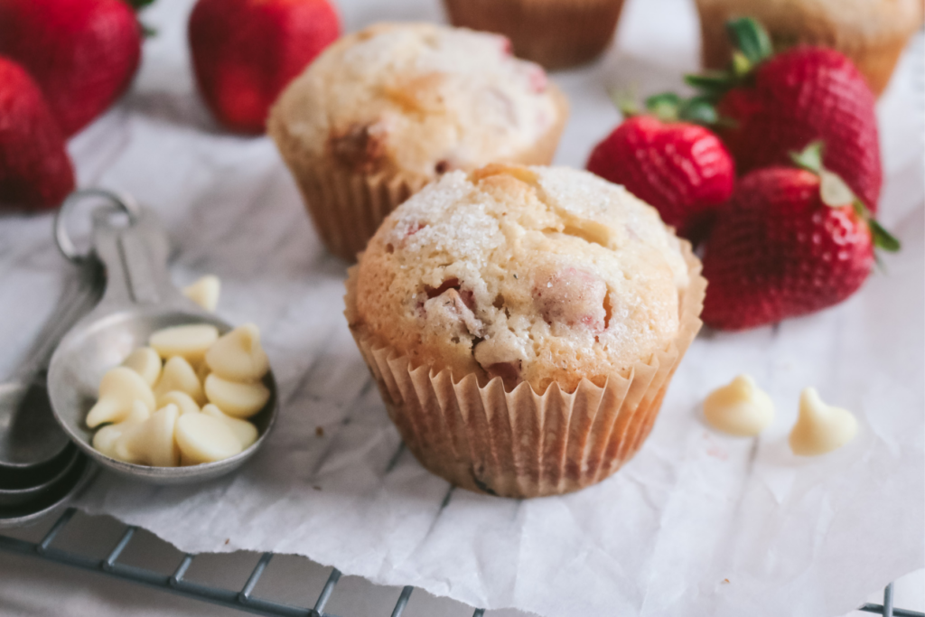 wire rack lined with parchment paper with white chocolate chips, fresh strawberries, and white chocolate strawberries muffins sprinkled with lavender sugar.