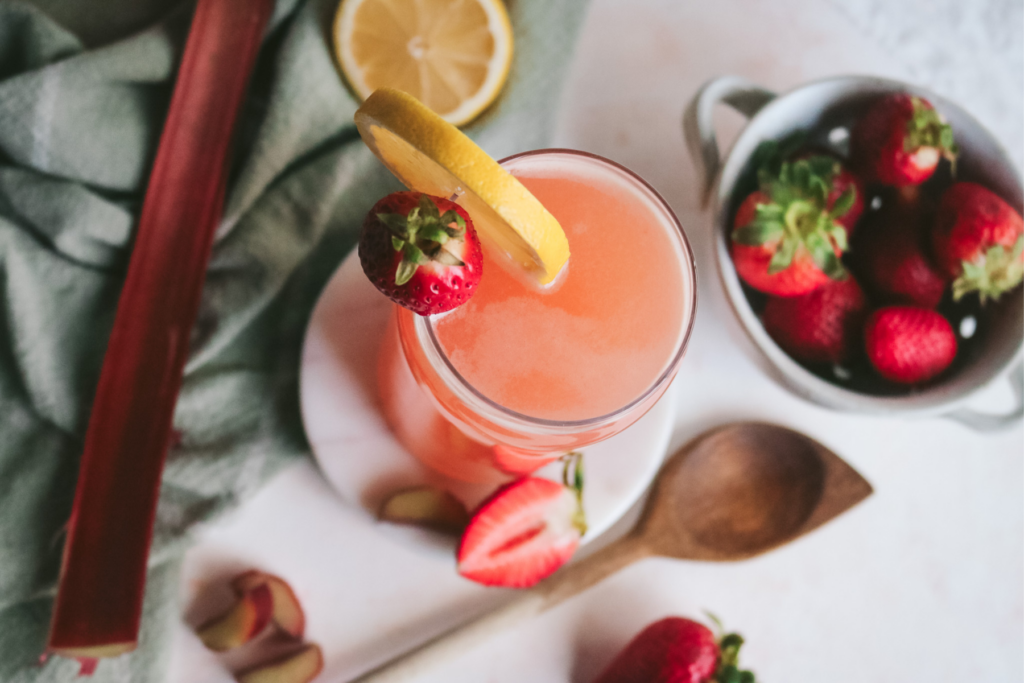 overhead view of a glass of strawberry rhubarb lemonade next to a bowl of strawberries and sliced rhubarb.