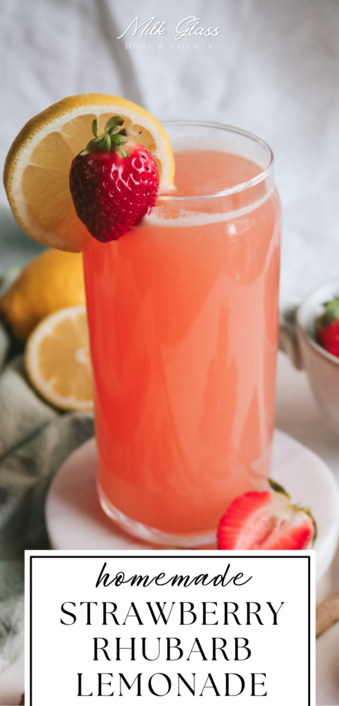 tall pin with a pink glass of strawberry rhubarb lemonade topped with a slice of strawberry and lemon.