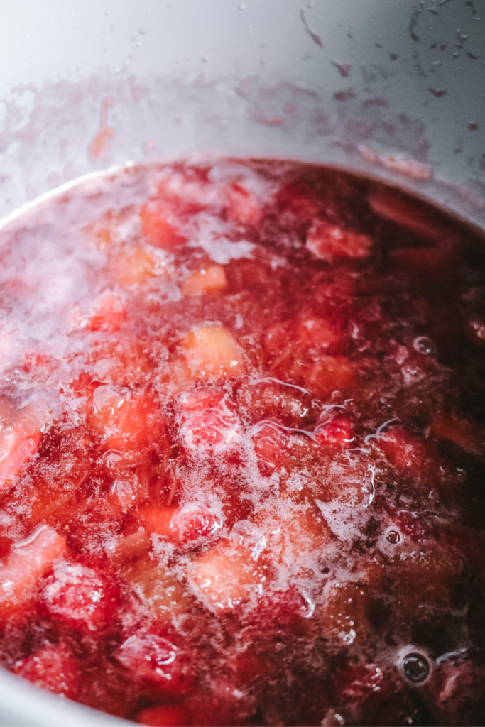 mixture of strawberry and rhubarb syrup bubbling in a pan.