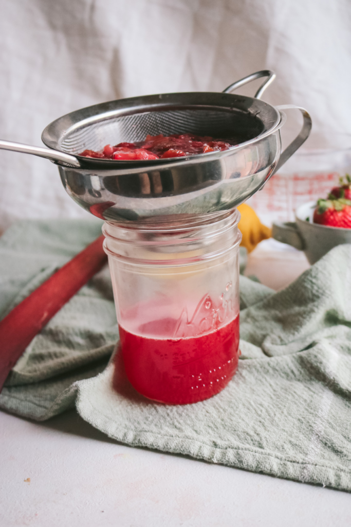 straining strawberry and rhubarb into a mason jar.