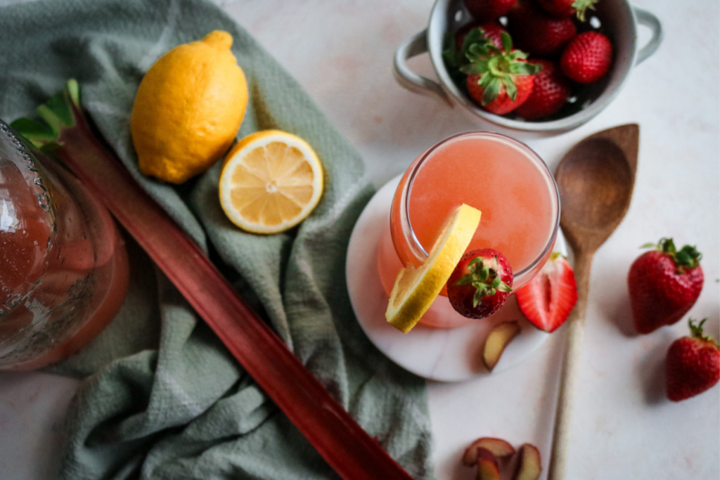 overhead view of a glass of homemade strawberry rhubarb lemonade next to fresh strawberries, rhubarb, and lemonade.
