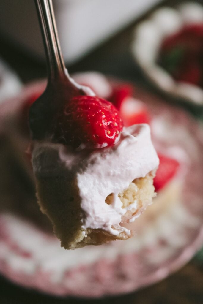 close up view of a fork with cake, strawberry whipped cream, and a fresh strawberry.