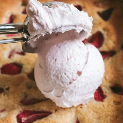 close up view of a scoop of creamy pink strawberry whipped cream being placed on a strawberry cake.