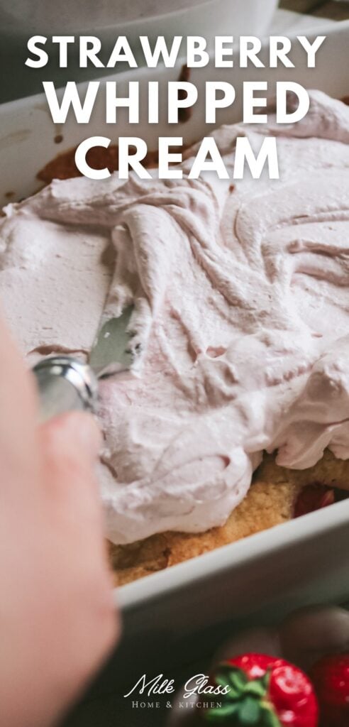 hand spreading strawberry whipped cream on a cake.