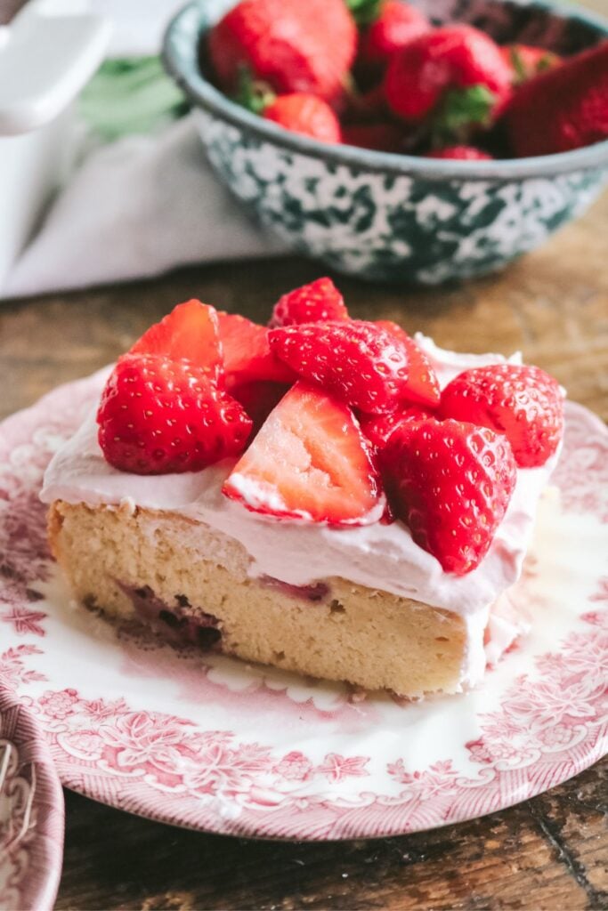 slice of strawberry snack cake with fresh strawberry whipped cream on top.
