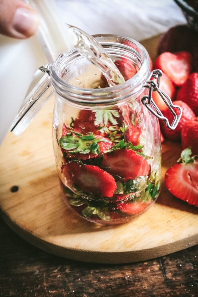 pouring rice vinegar in a glass jar of strawberry tops.