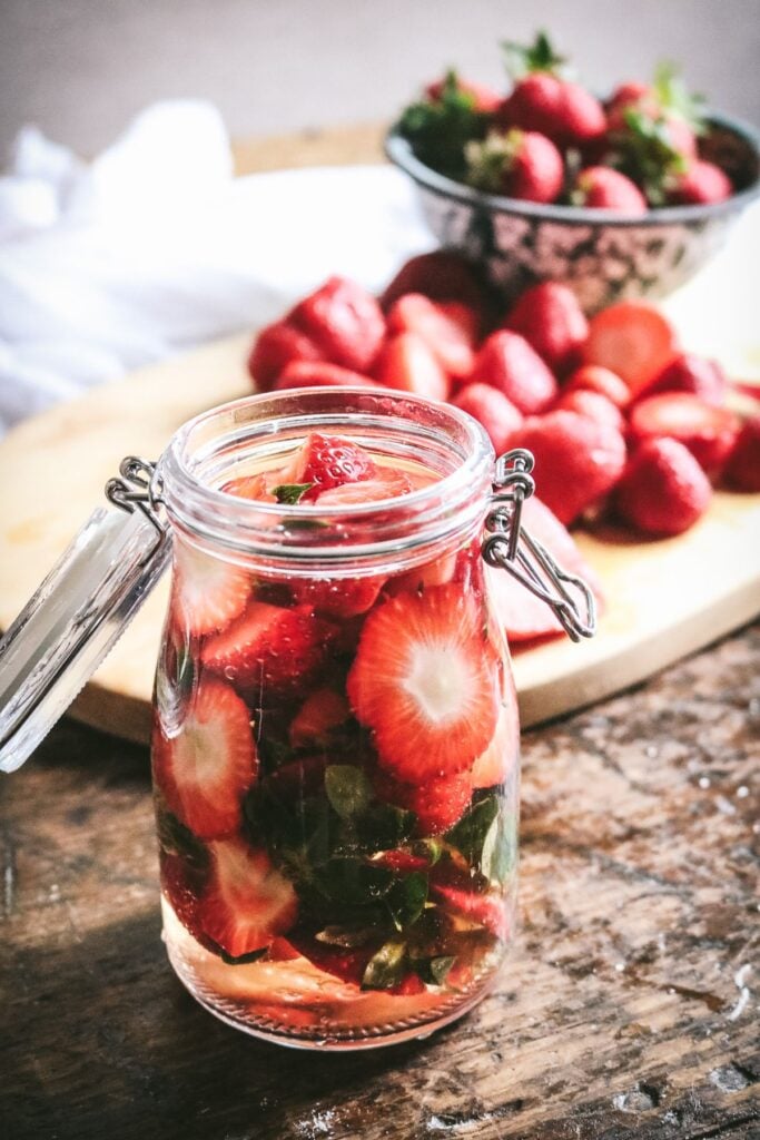 glass jar with strawberry tops floating in rice vinegar.