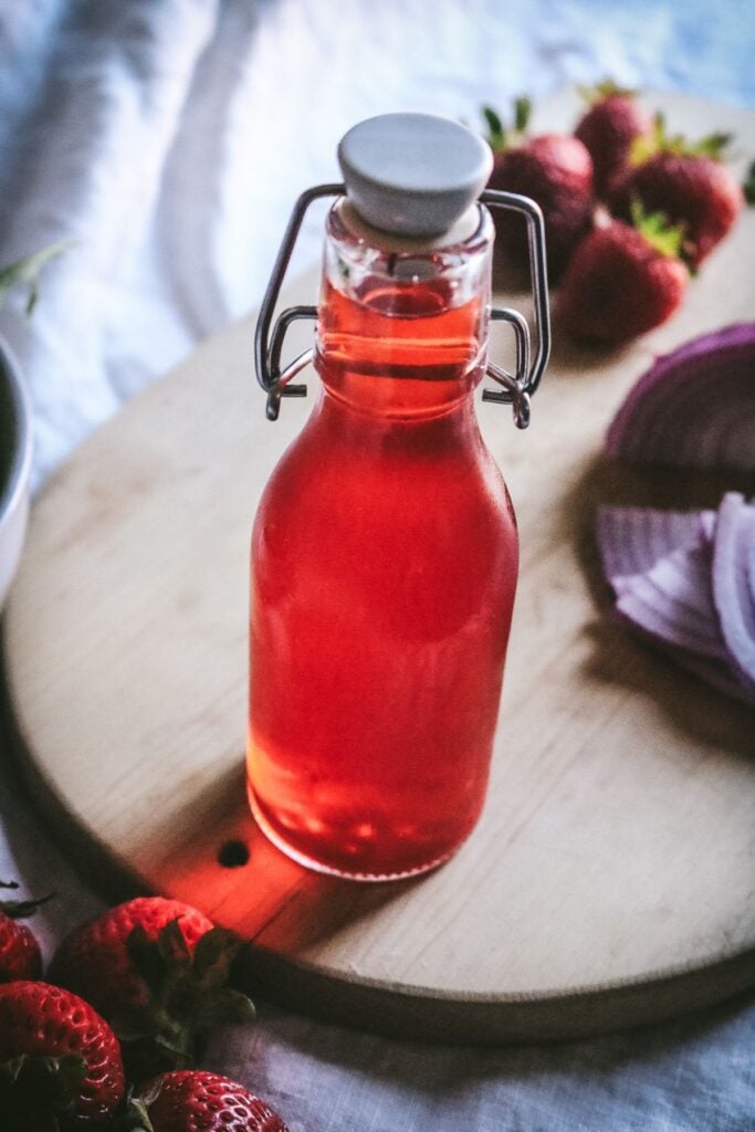 angled view of strawberry top infused vinegar with light coming through the red liquid.