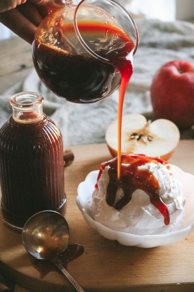 pouring apple cider syrup over a bowl of whipped cream for a garnish.