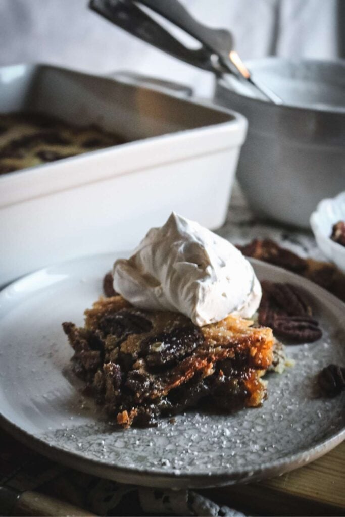 serving of pecan cobbler on a plate with whipped cream on top.