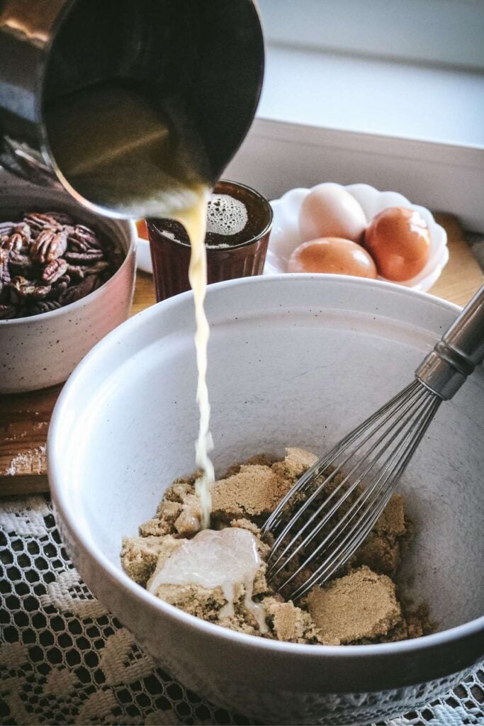 pouring butter into brown sugar for pecan pie filling.