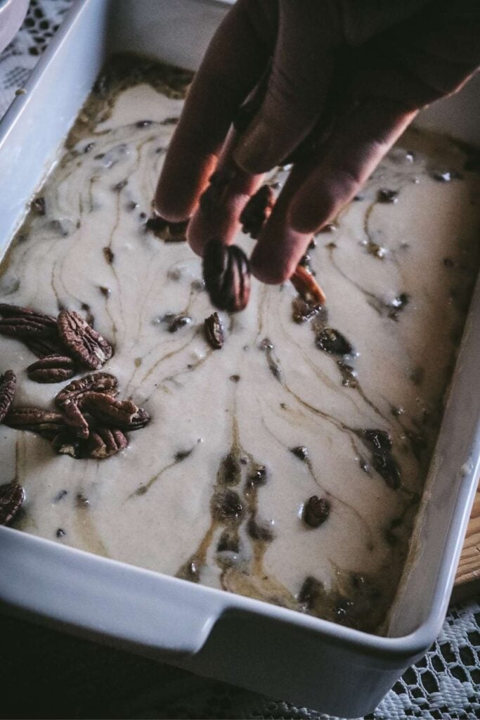 sprinkling pecans over a baking dish layered with pecan pie filling and cobbler topping.