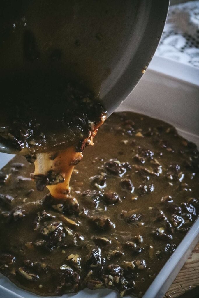 pouring pecan pie filling in a ceramic baking dish for cobbler.