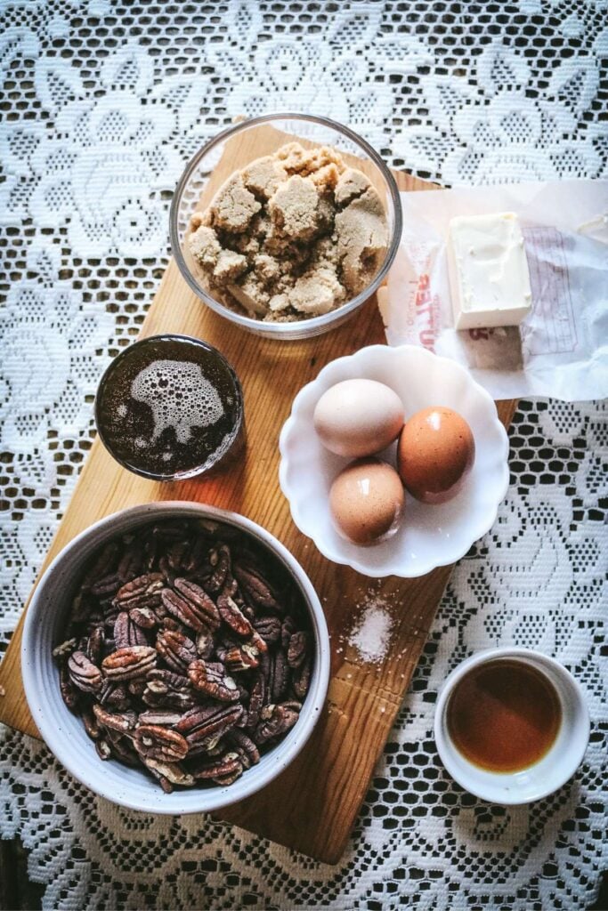 overhead view of the ingredients for pecan pie cobbler including maple syrup, eggs, butter, brown sugar, bourbon vanilla extract, and lots of pecan halves.