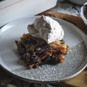 scoop of pecan pie cobbler topped with lots of whipped cream on a plate.