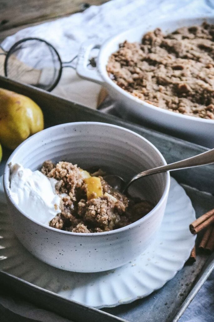 close up view of homemade pear crumble with whipped cream next to fresh pears.