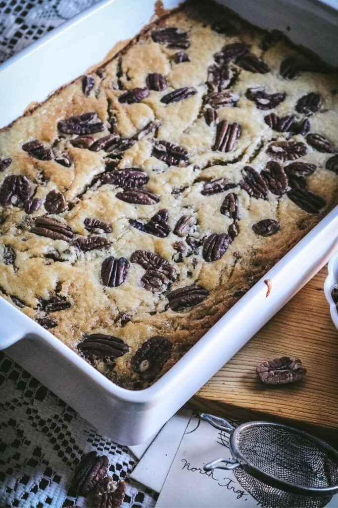 white baking dish with homemade pecan pie cobbler with lots of pecans on top.