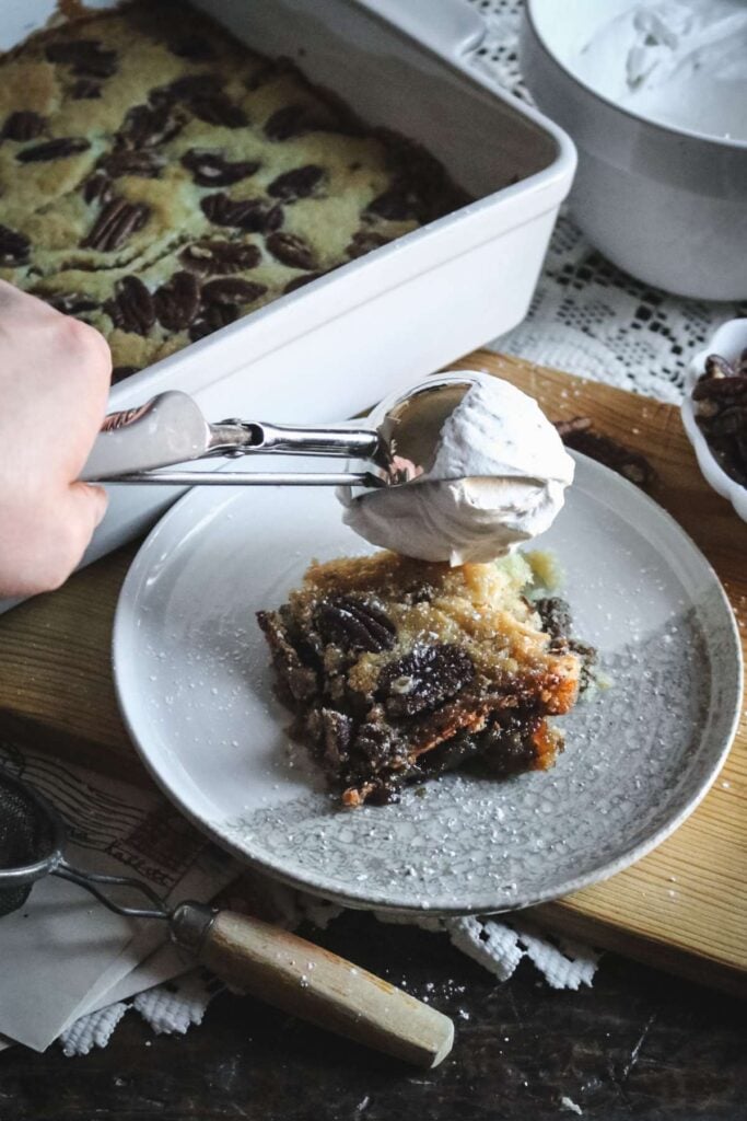 dolloping a scoop of whipped cream on a serving of pecan cobbler.