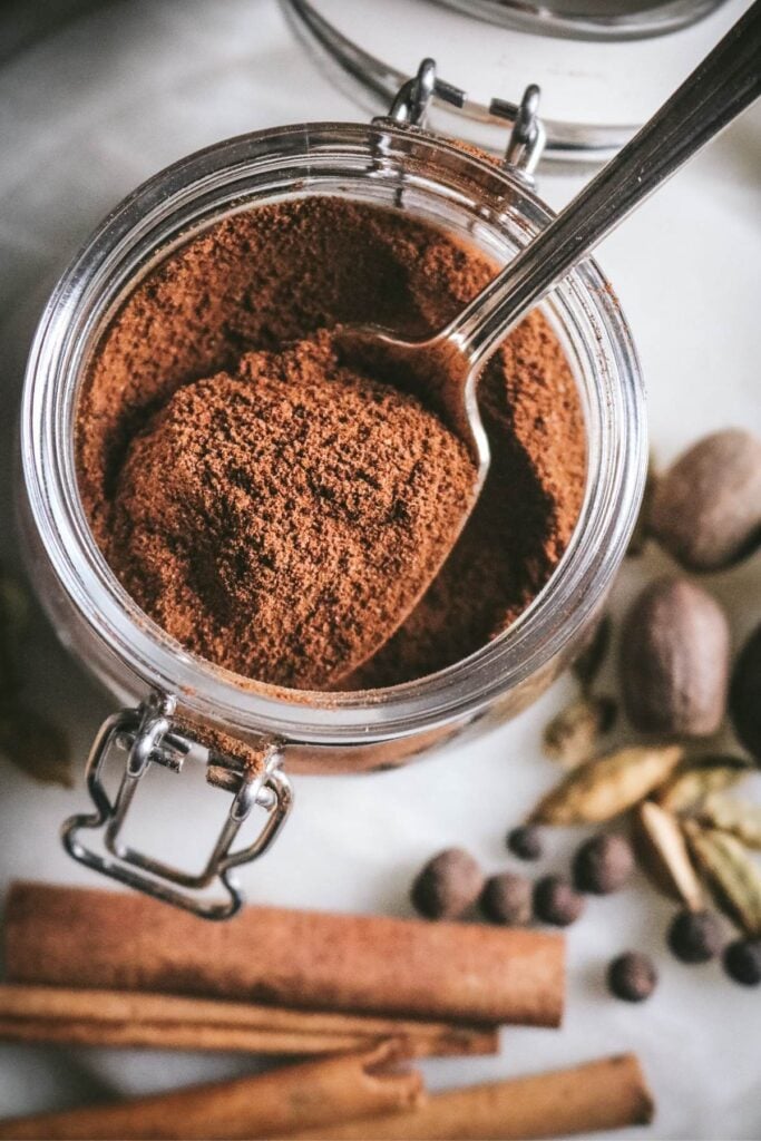overhead view of a glass jar with homemade apple pie spice made with cardamom, cinnamon, allspice, nutmeg, and ginger.