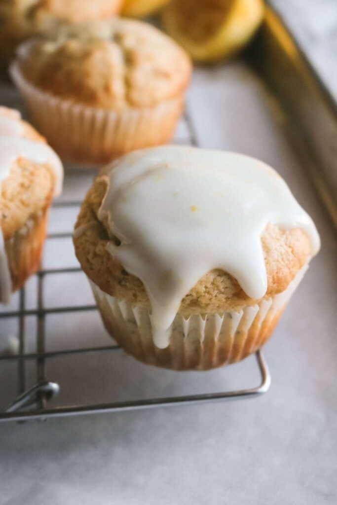 thick lemon glaze dripping down the sides of a muffin on a wire rack.