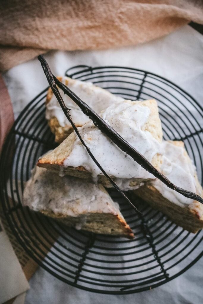 overhead view of vanilla bean scones stacked on a wire rack with a sliced vanilla bean on top.