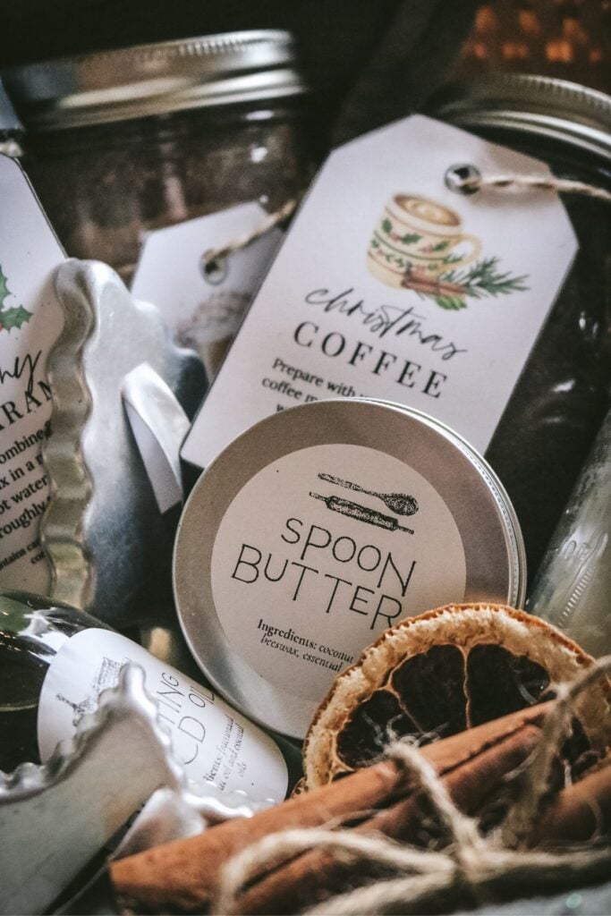 close up image of different homemade christmas gift ideas with printable tags arranged artfully in a handmade basket with dried orange slices, cinnamon sticks, and a kitchen towel.