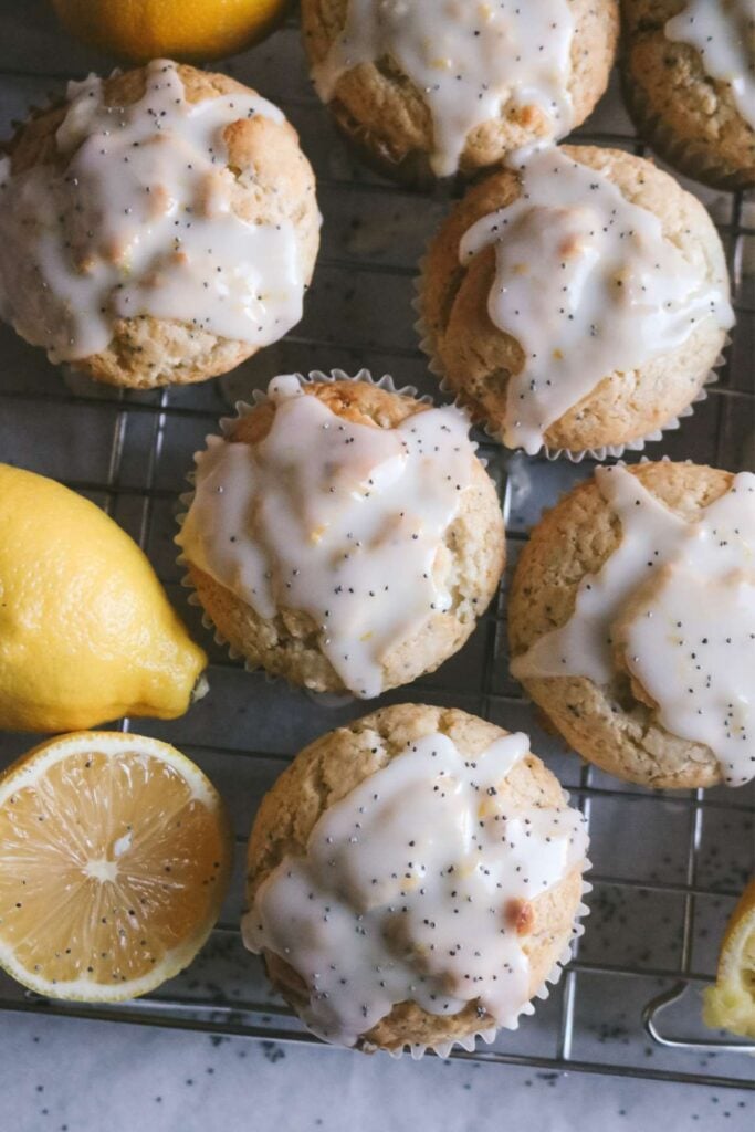 overhead view of glazed lemon and poppy seed muffins cooling on a wire rack next to fresh lemons.