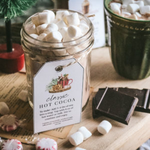 mason jar with homemade hot cocoa mix with a printable label tied to the front and marshmallows on top.