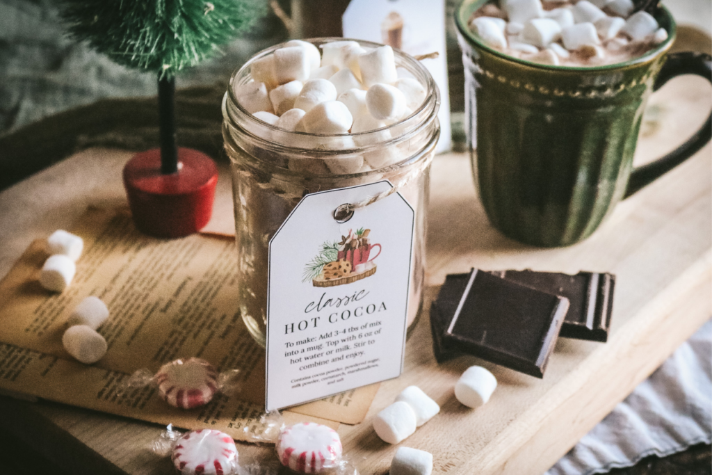 wide view of a jar of homemade hot cocoa mix next to peppermint candies, dark chocolate, and a mug of hot cocoa.