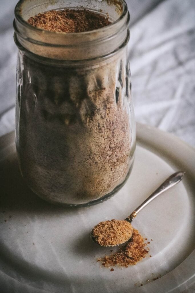 metal spoon with homemade caramel sugar on a marble base next to a jar of ground caramel sugar.