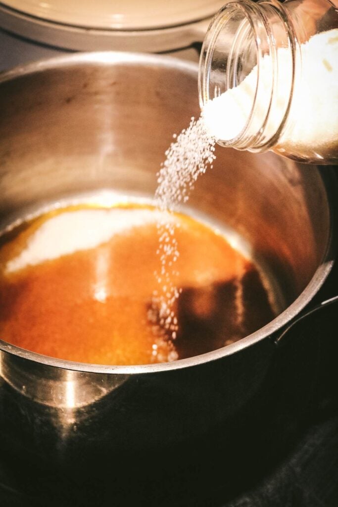 adding more sugar to caramel in a pan.
