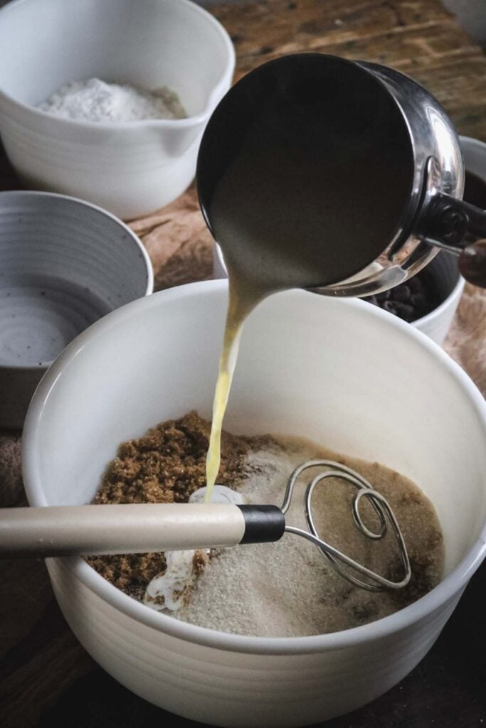 pouring melted butter into a milk glass mixing bowl of brown and white sugar.