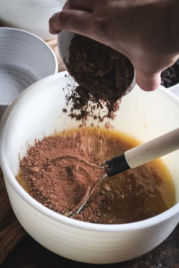 sprinkling cocoa powder into chocolate chocolate chip cookie bar dough.