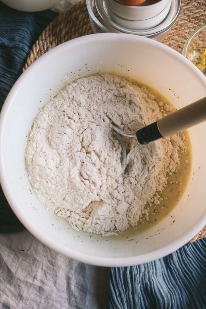 adding flour and dry ingredients to muffin batter for lemon poppyseed muffins.