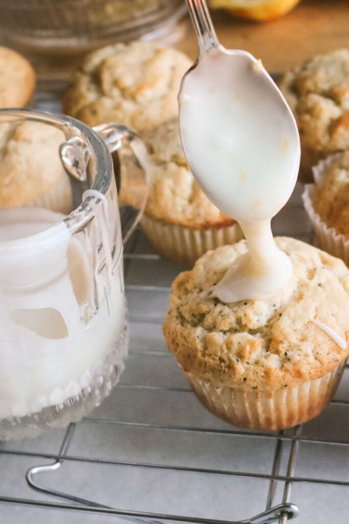 drizzling lemon glaze over lemon poppyseed muffins on a wire rack.