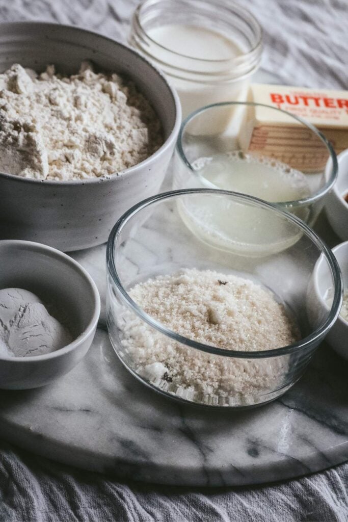 marble tray with the ingredients to make vanilla bean scones like vanilla sugar, butter, flour, and cream.