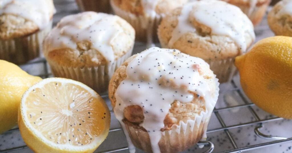 collection of homemade lemon and poppy seed muffins cooling on a wire rack next to a half lemon.