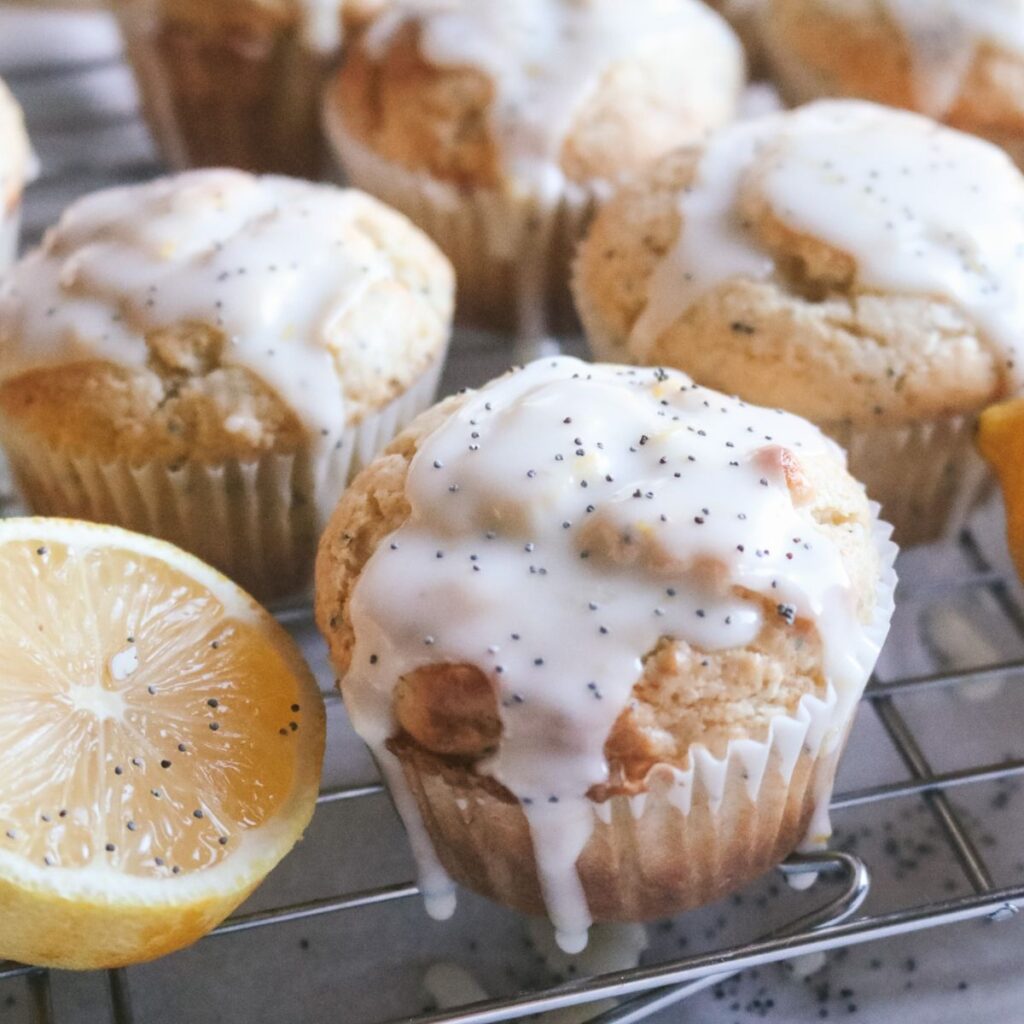 close up view of glazed lemon poppyseed muffins on a wire rack with poppyseeds sprinkled over top.