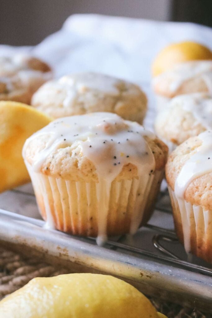 side view of a fresh poppyseed lemon muffin cooling on a wire rack with homemade lemon glaze drizzled on top.