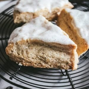 close up of a vanilla scone with vanilla bean glaze on a wire rack.
