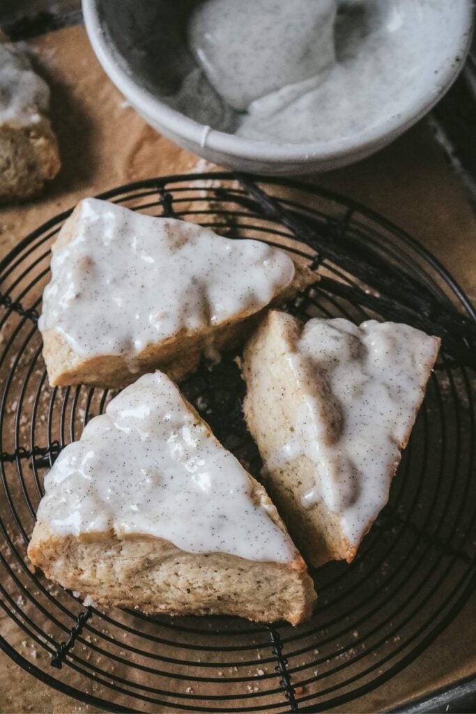 three glazed vanilla bean scones cooling on a wire rack next to a bowl of vanilla bean glaze.