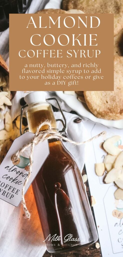 a glass bottle of homemade almond flavored simple syrup on a white cloth next to sliced almonds, printable gift tags, and shortbread cookies.