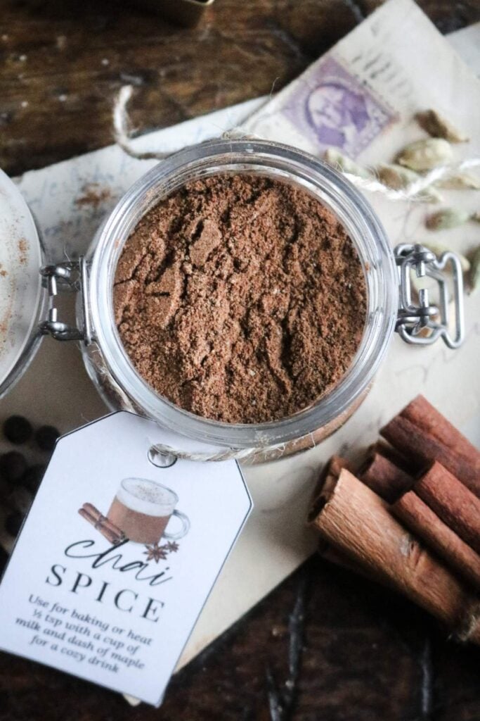 overhead view of a glass spice jar with a chai spice label next to dried cinnamon sticks and cardamom pods.