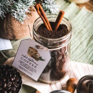 overhead view of a mason jar with homemade spiced coffee for christmas with a printable label, cinnamon sticks, and a christmas tree in the back.