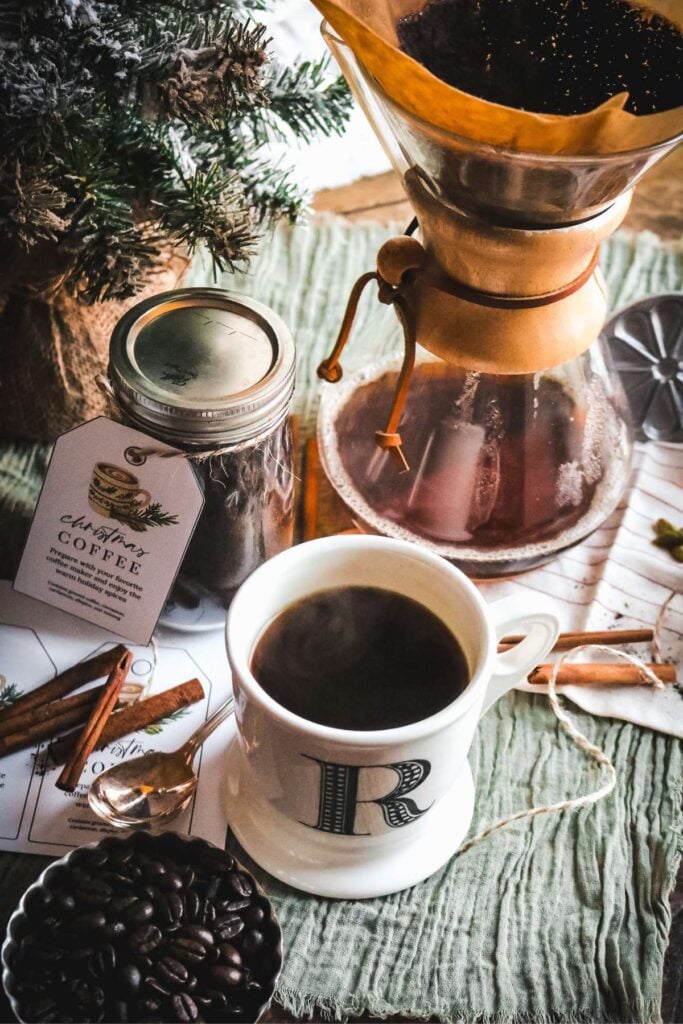 mug of homemade christmas coffee with steam coming off of it and a chemex and a jar of homemade spiced coffee in the back.