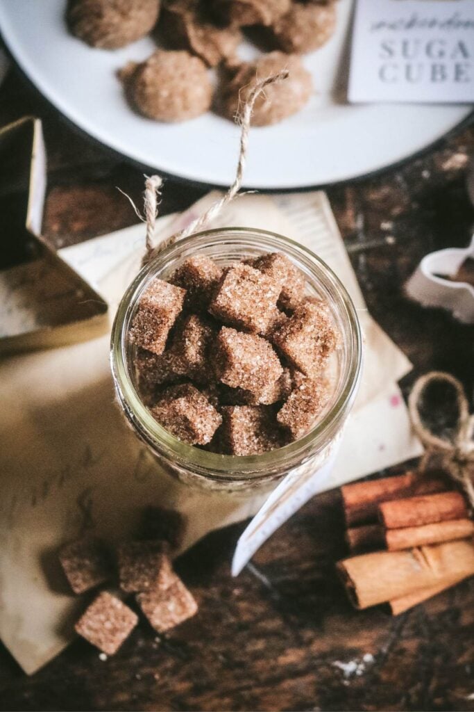 overhead view of a mason jar with homemade brown sugar cubes next to a plate with ornament-shaped sugar for holiday gifting.