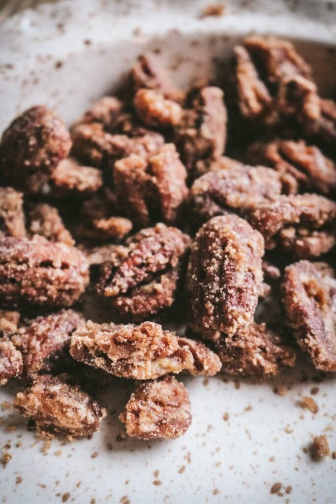 close up of crunchy sugary maple pecans in a speckled brown and white ceramic pie plate.