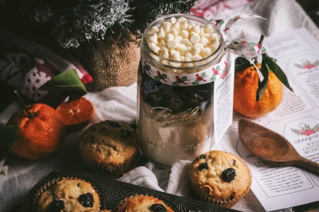 scene with freshly baked cranberry muffins, a jar of cranberry muffin mix, fresh oranges, and printable labels to attach to jars for easy gifting.