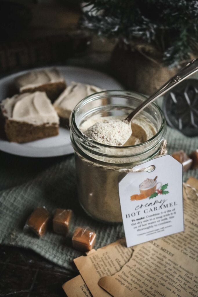 a pint mason jar with homemade hot caramel milk mix with a spoon sticking out of the jar and a plate of gingerbread blondies in the background.